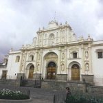FACHADA DE LA CATEDRAL DE ANTIGUA GUATEMALA QUE ES LA IGLESIA PRINCIPAL Y ES DE COLOSAL TAMAÑO es una fachada de colosal tamaño color blanca con tres puertas al frente viendo hacia la plasa central de antigua guatemala