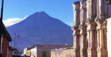 VISTA DESDE UNA CALLE DE ANTIGUA GUATEMALA DONDE SE APRECIA EL VOLCAN DE AGUA Y PARTE DE LA FACHADA DE USA IGLESIA QUE SE LLAMA DEL CARMEN